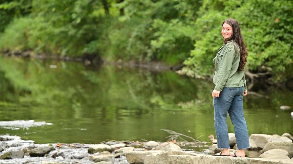 woman walks along rocks on river's edge