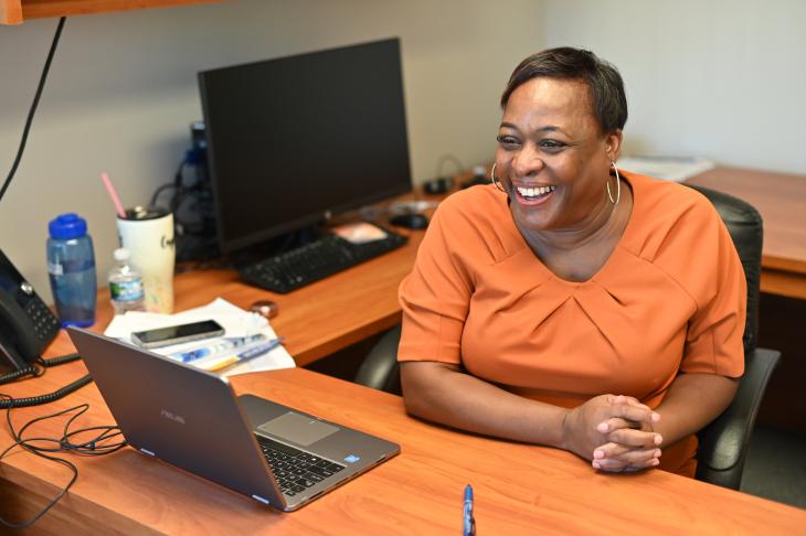 Smiling black female wearing orange blouse seated at desk